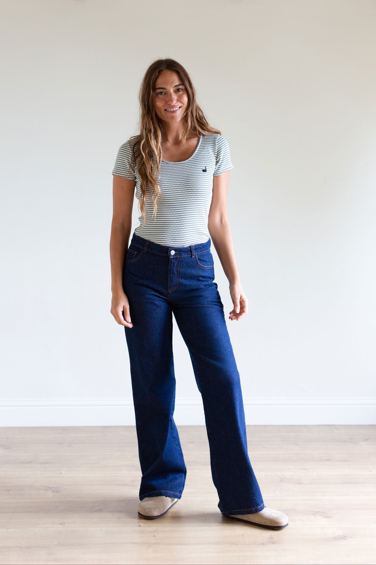 Full body view of a woman in a sage green striped ribbed top and wide-leg jeans.