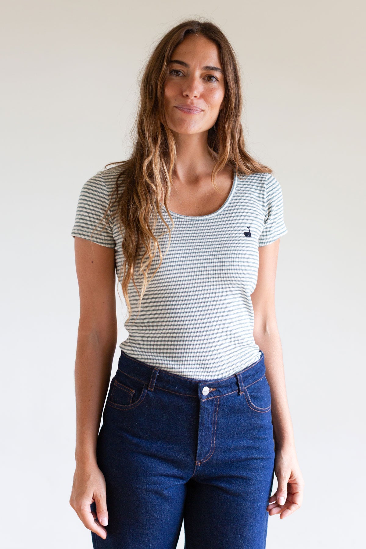 Woman wearing a sage green striped slim-fit ribbed shirt and blue jeans.
