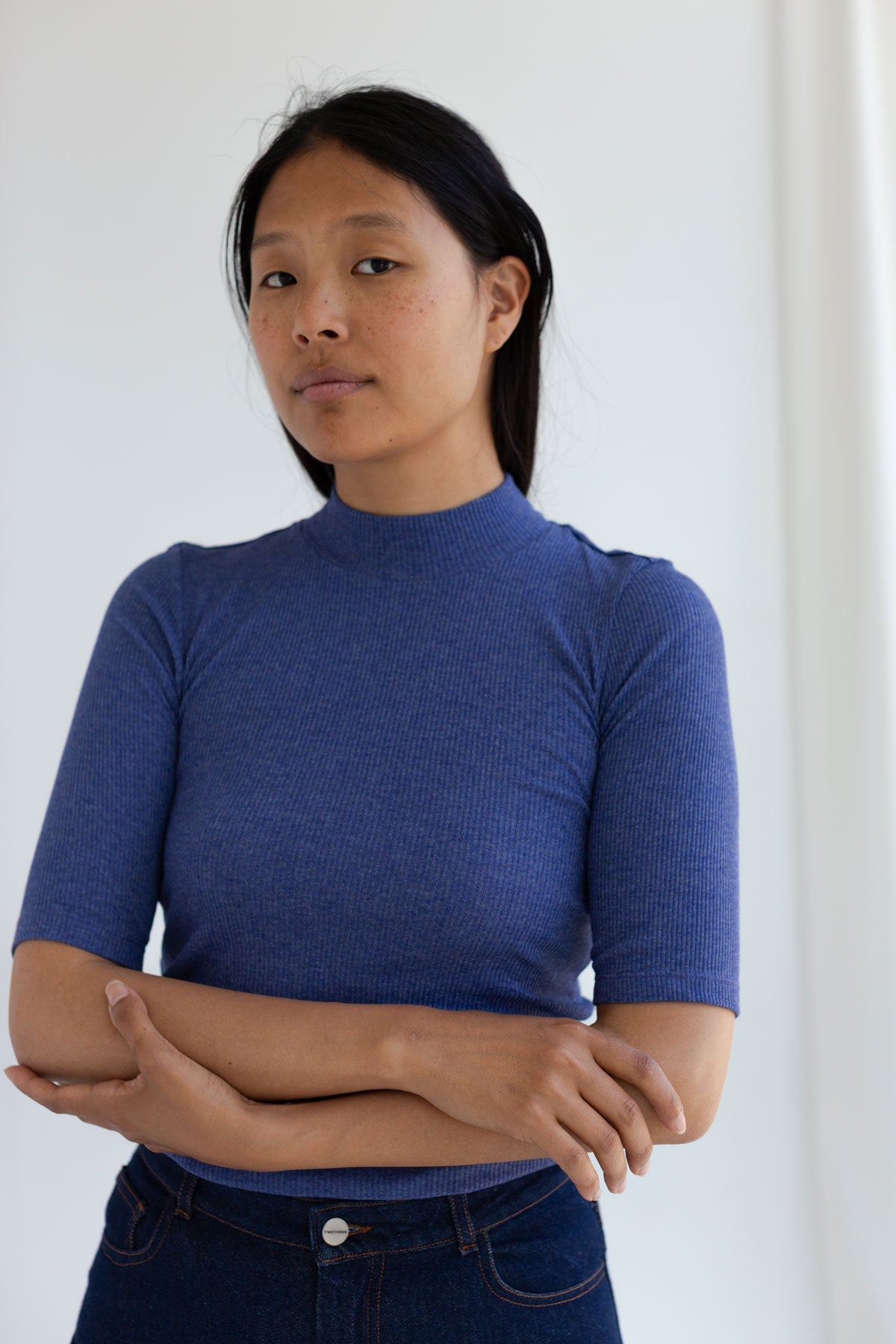 Woman with arms crossed wearing a mazarine blue mock-neck ribbed top.